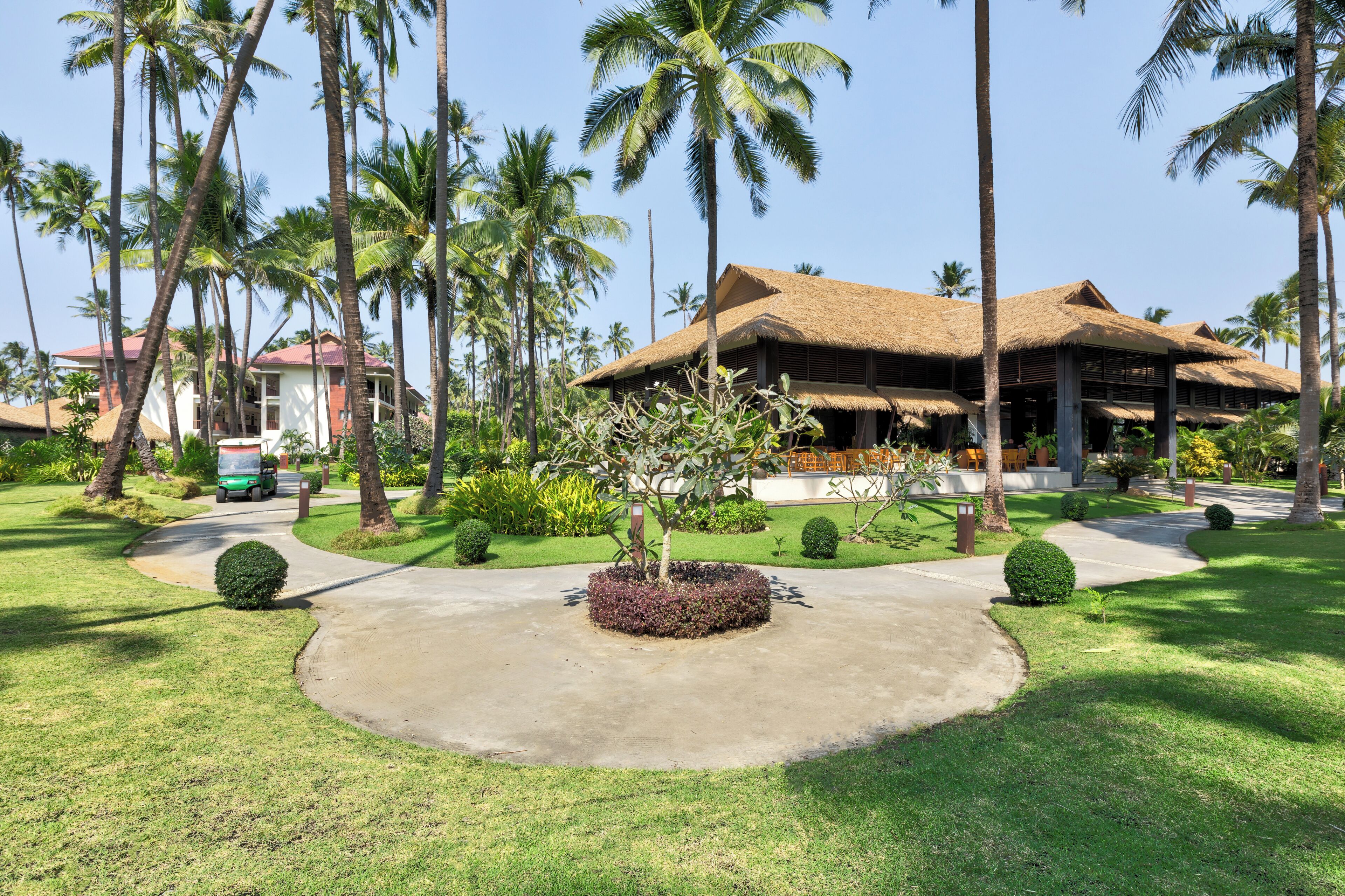 Resort com construção de telhado de palha, cercado por palmeiras e gramados bem cuidados.