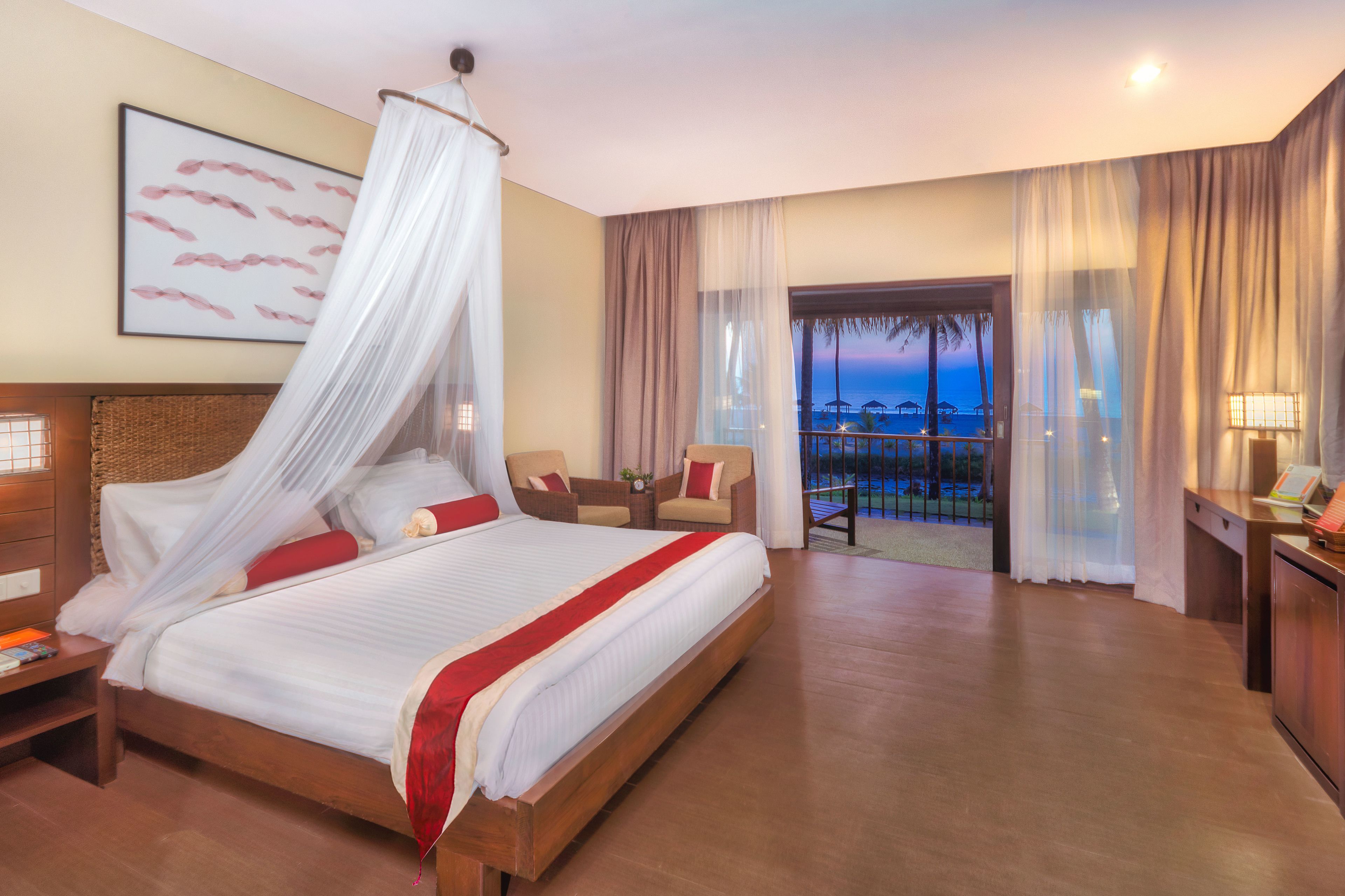 A hotel room with a large bed, a balcony with a view, and a desk with a lamp.