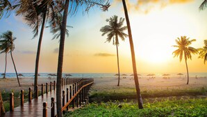 A wooden deck leading to a beach with palm trees and beach umbrellas. - Eskala Hotels & Resorts Ngwe Saung (Ngwe Saung)