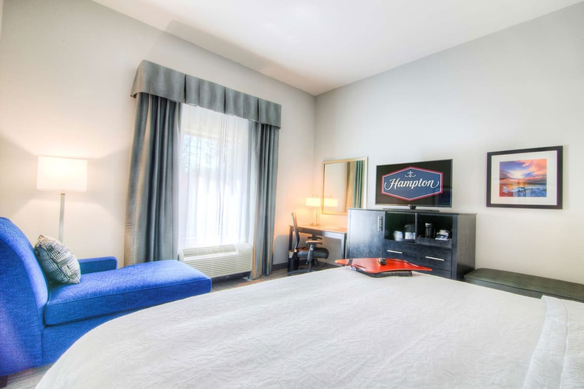 Una habitación de hotel con cama, escritorio, silla, televisor y ventana con cortinas.
