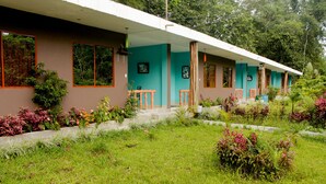 A building with a covered walkway, large windows, and a garden with various plants.