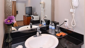 Een hotelbadkamer met een witte wastafel, een spiegel, een haardroger, een telefoon en toiletartikelen op het aanrecht.