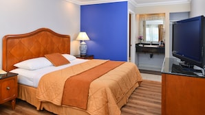 Hotelkamer met een houten bed, nachtkastje, lamp, televisie, badkamer met wastafel en spiegel, en een blauwe accentmuur.