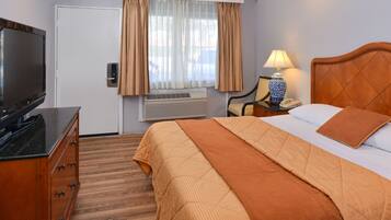 A hotel room with a bed, a TV, a desk with a lamp, and a window with curtains.