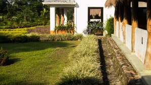A white building with a thatched roof, surrounded by a well-maintained garden with various plants and a stone pathway. - Cinaruco Caney (Villavicencio)