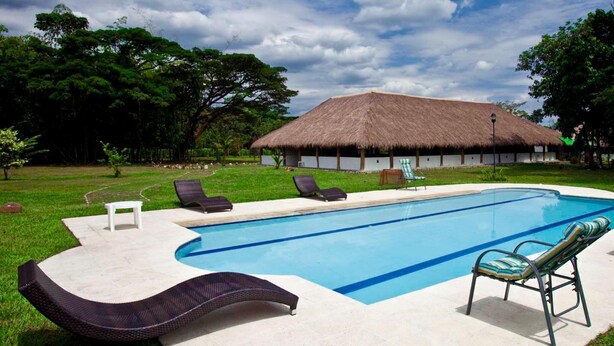 A swimming pool with lounge chairs, a thatched-roof building, and lush greenery. - Cinaruco Caney (Villavicencio)