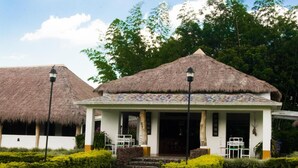 A thatched-roof building with a tiled porch and a garden with red flowers and rocks. - Cinaruco Caney (Villavicencio)