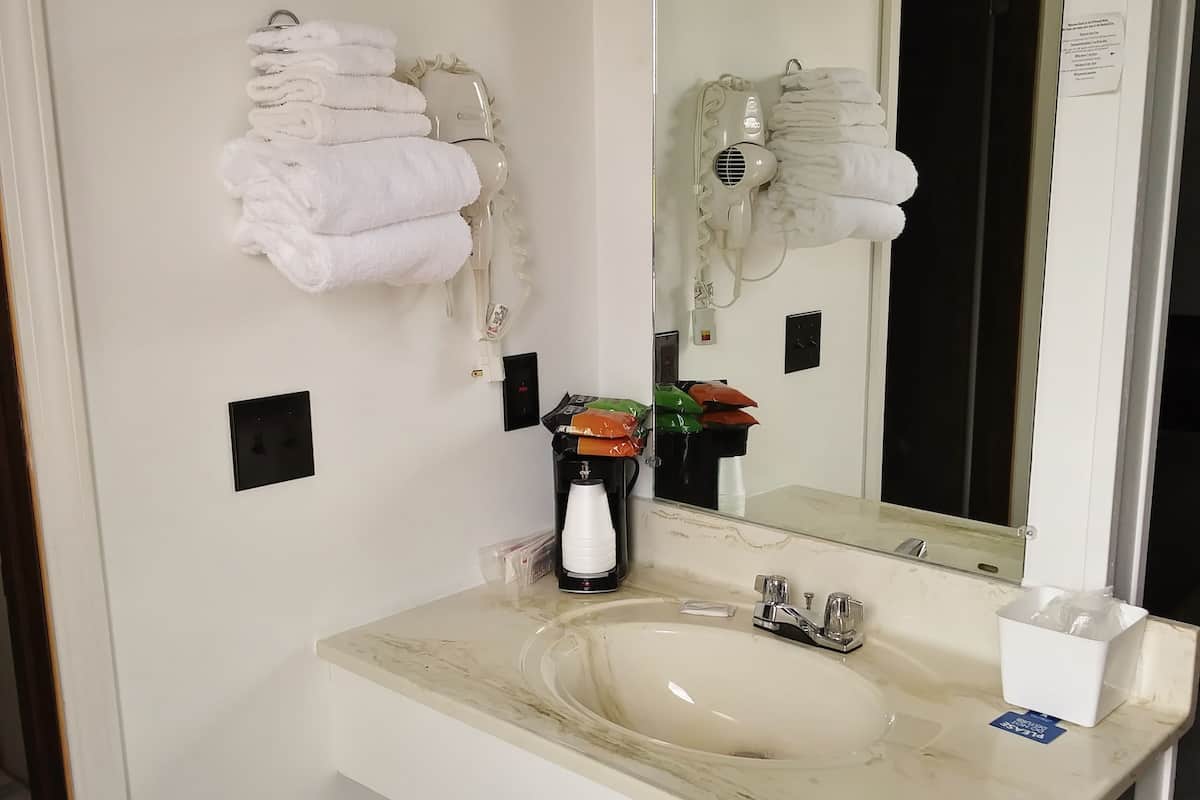 A bathroom with a sink, mirror, towel rack, and a trash bin.