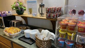 Een ontbijtbuffet met diverse etenswaren, zoals cornflakes, yoghurt en koffie.