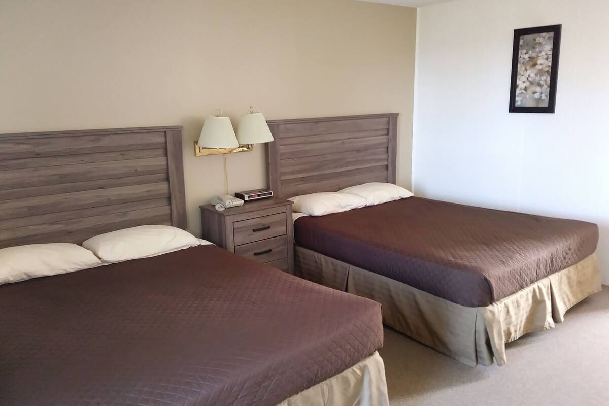 A hotel room with two beds, a nightstand with lamps, and a framed picture on the wall.