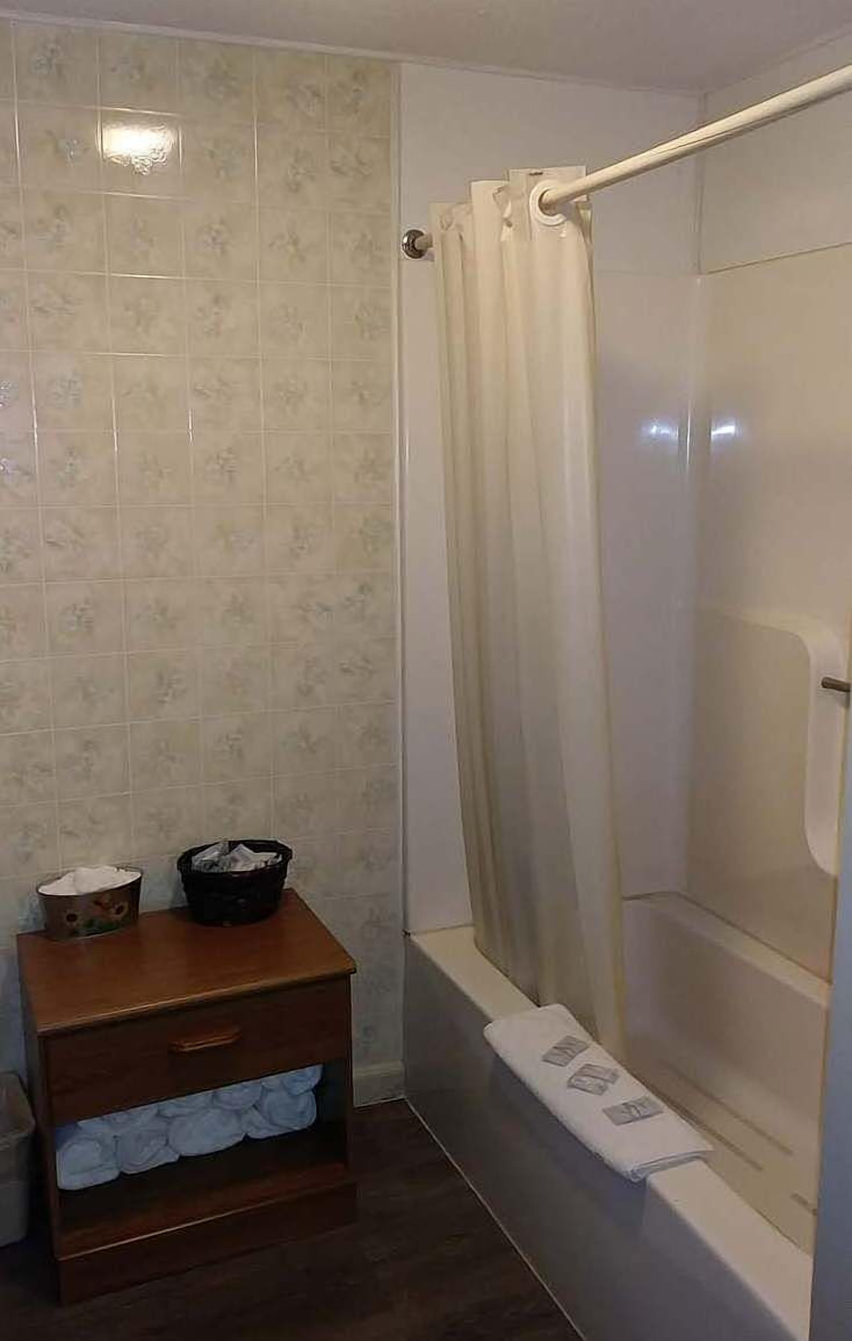A bathroom with a shower, a wooden cabinet with towels, and a tiled wall.