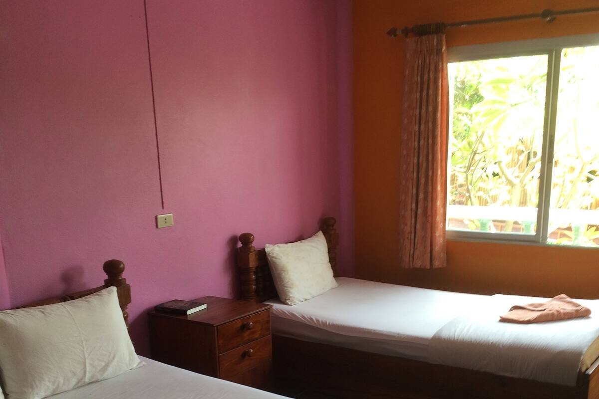 A room with two beds, a wooden nightstand, and a window with curtains.