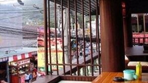 A restaurant with a wooden table and chairs, a view of the street outside, and a hanging light fixture. - Baan Talay Guesthouse & Dormitory (Ko Pha-ngan)