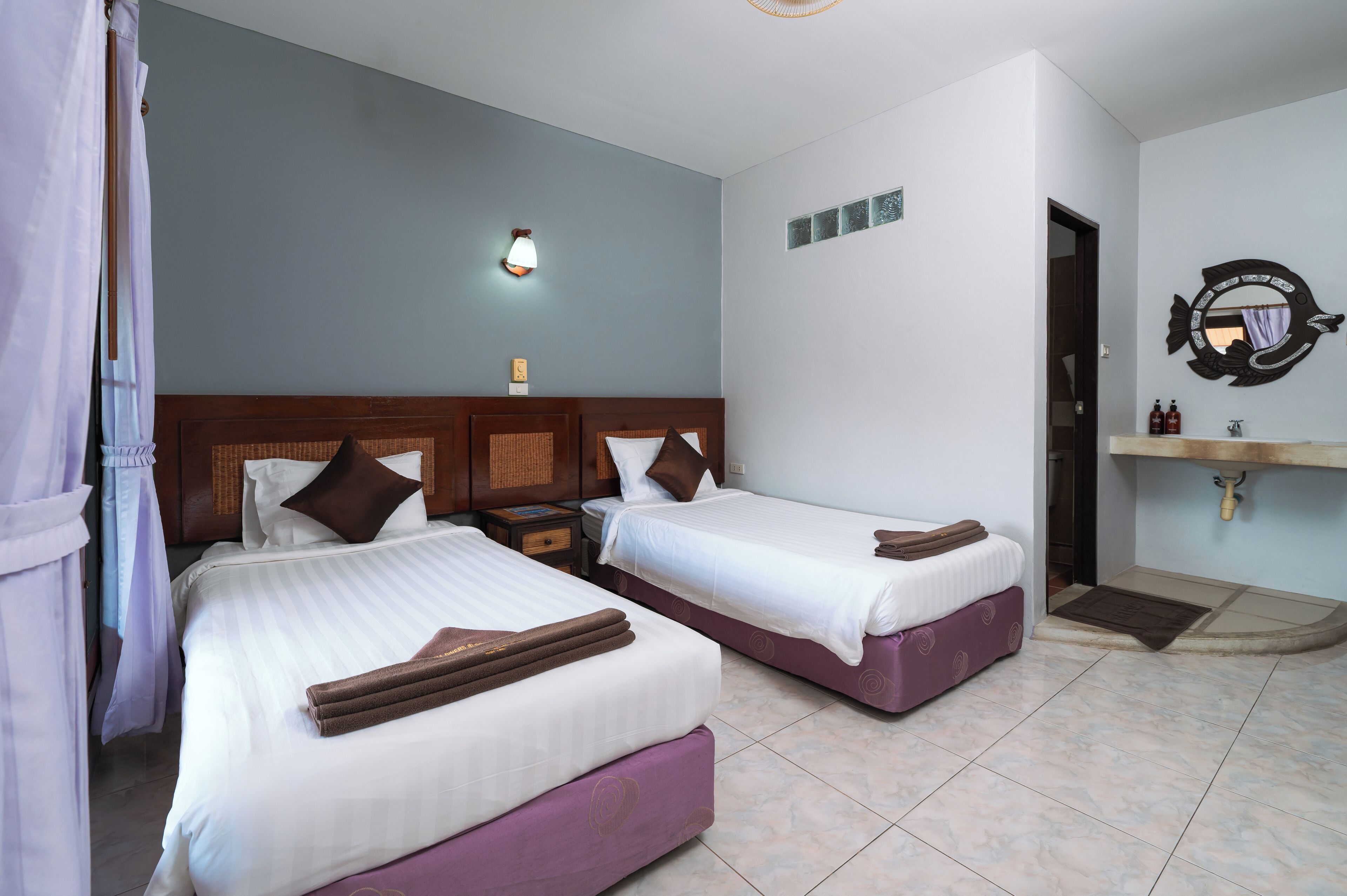 Ein Hotelzimmer mit zwei Betten, einem Nachttisch, einer Wandleuchte, einem Spiegel und einem Badezimmer mit Waschbecken und Spiegel.