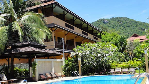A swimming pool with lounge chairs, a covered area, and a mountain in the background. - Asia Divers Resort (Koh Tao)