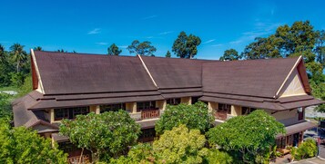 A traditional multi-story building with a sloped roof, surrounded by lush greenery and trees.