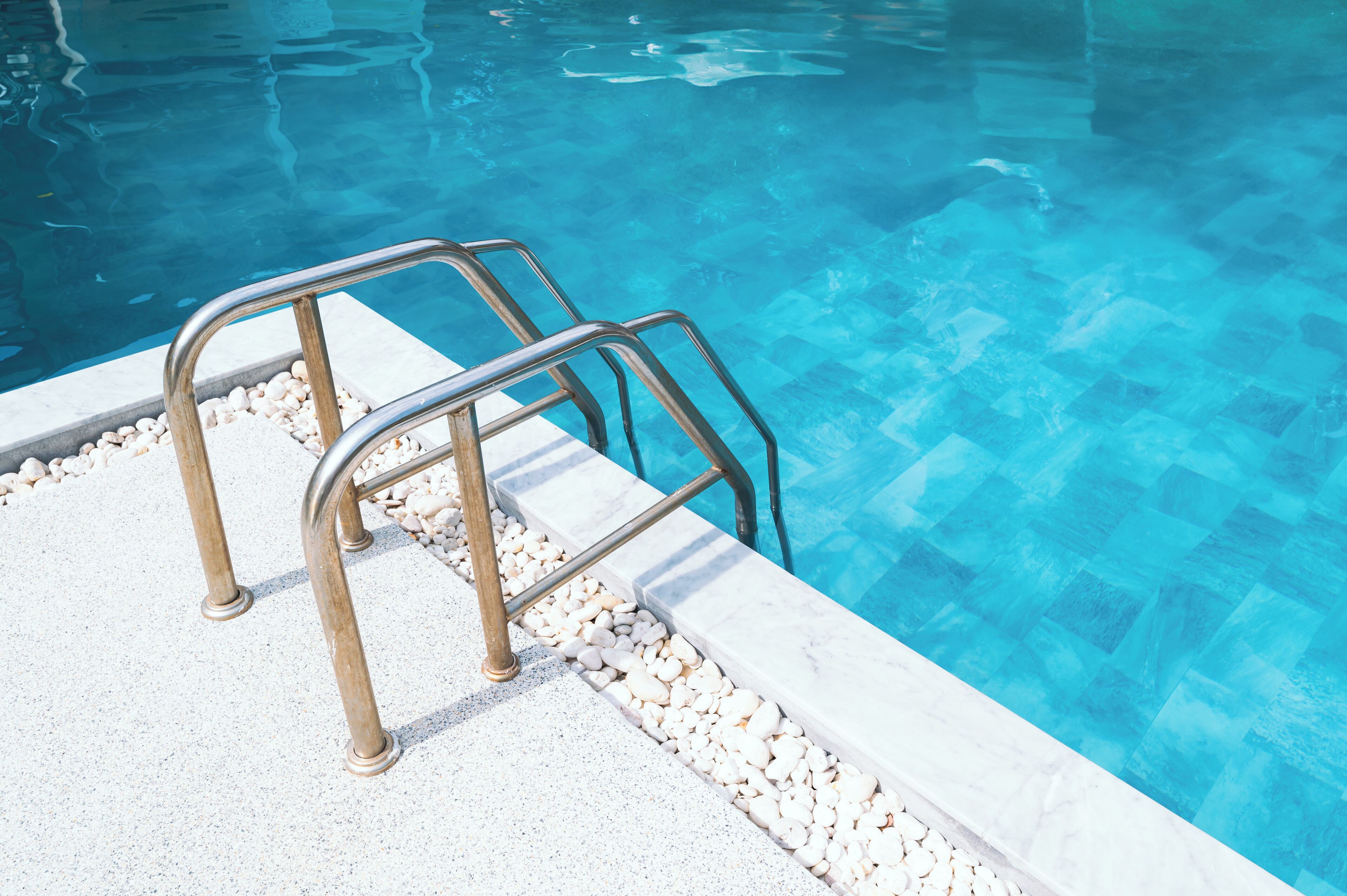 A poolside area with metal pool ladders and a pebble-lined edge.
