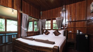 A wooden-framed bed with white linens, a small black refrigerator, and a window with curtains. - Asia Divers Resort (Koh Tao)