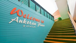 A staircase leading up to a teal wall with a 'Welcome to Auktan Place' sign. - Aukotan Place Hotel (Koh Tao)