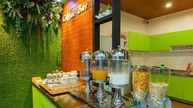 A breakfast bar with a wooden wall and green cabinets, featuring a coffee station with dispensers and a variety of food items. - Aukotan Place Hotel (Koh Tao)