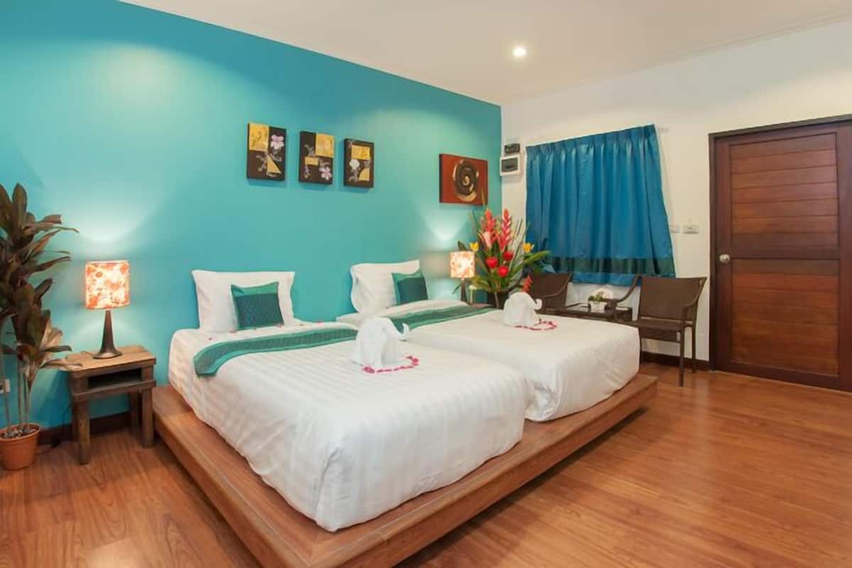 Une chambre avec deux lits, un bureau, une chaise, une plante en pot et des œuvres d’art accrochées au mur.