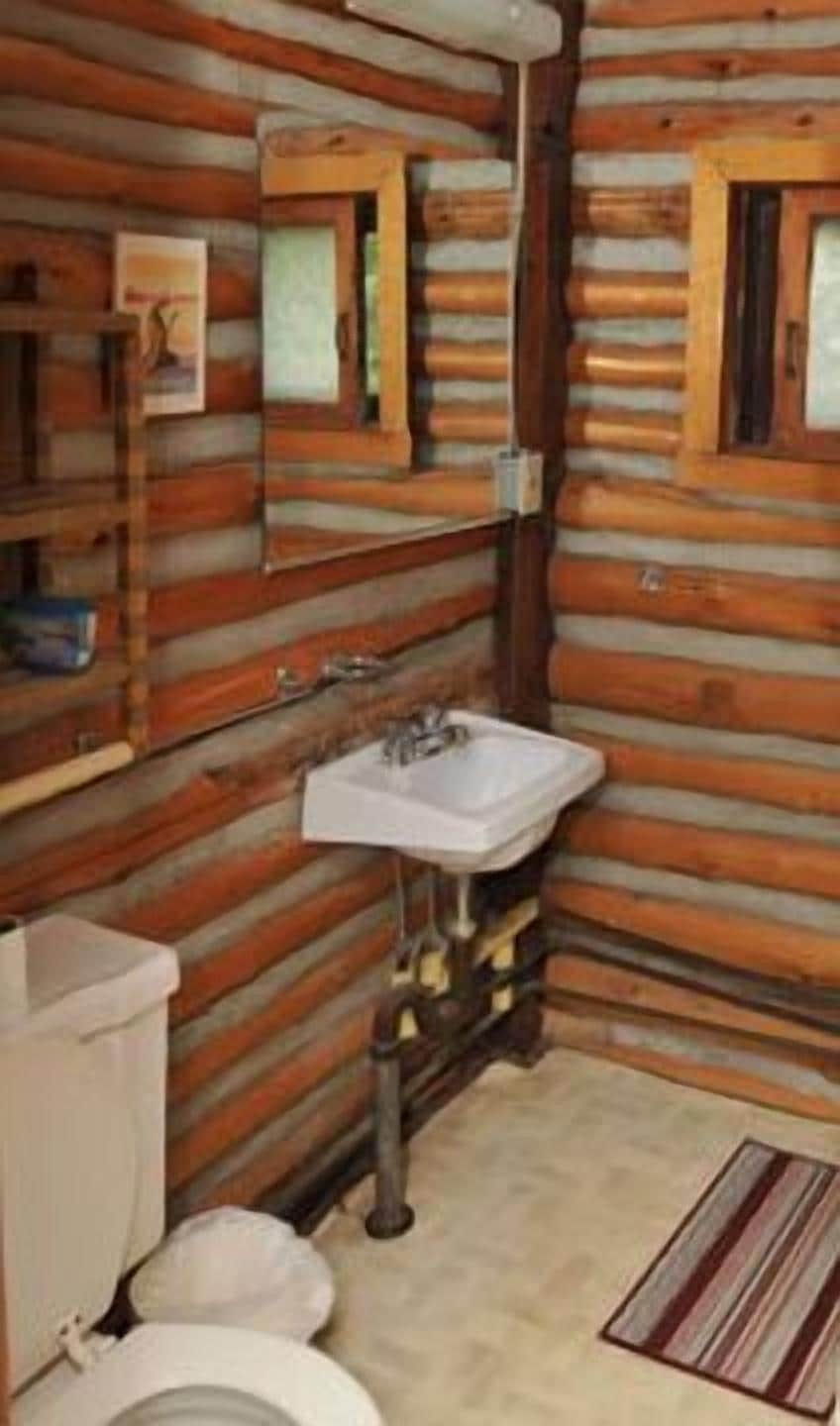 Une salle de bain rustique, aménagée dans une cabane en rondins, avec un lavabo, un miroir et des toilettes.