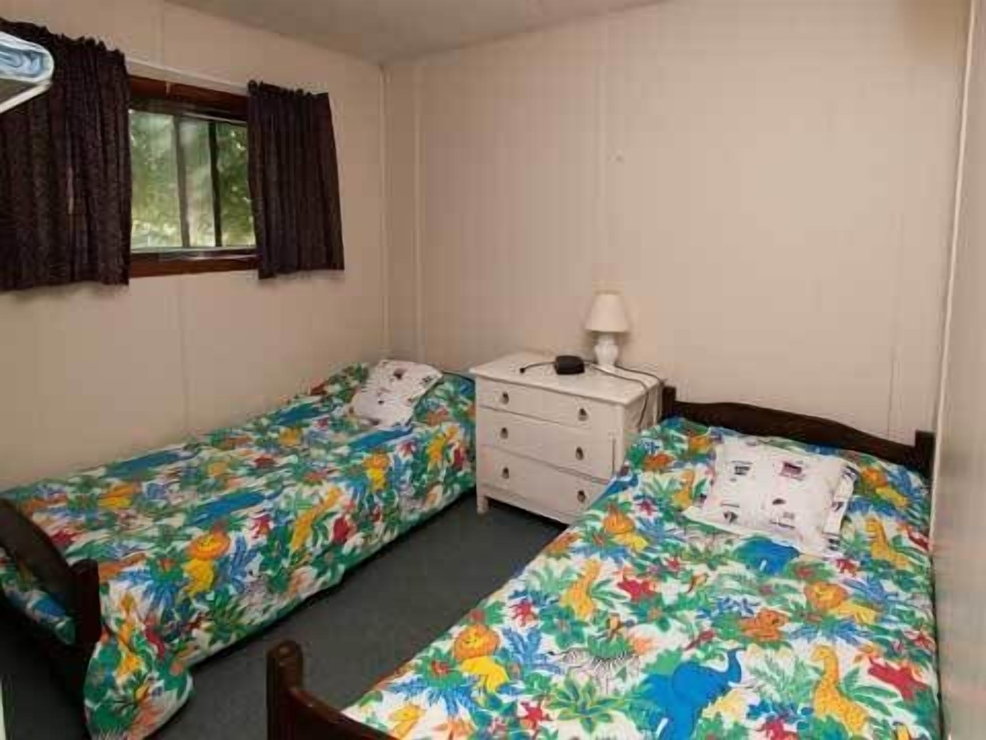 Una habitación pequeña y limpia con dos camas individuales, un aparador y una ventana con cortinas.