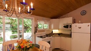 A kitchen with white cabinets, a stove, a microwave, and a refrigerator. There is a dining table with chairs and a vase of flowers.