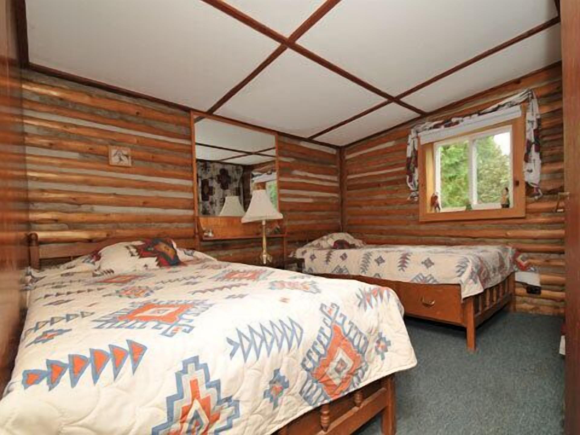 Una cabaña con dos camas de madera, una ventana con vistas a la vegetación y un techo con vigas de madera.