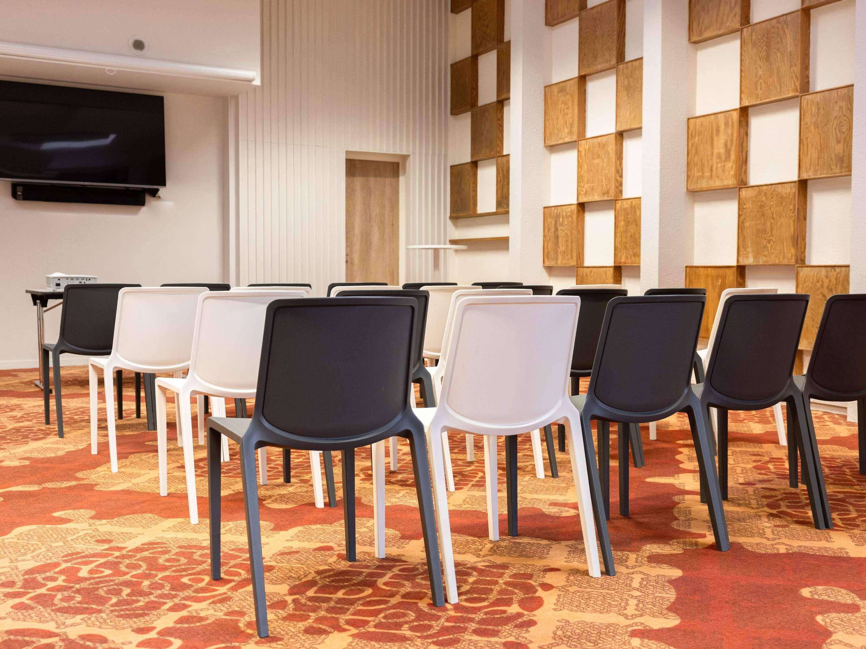 A conference room with rows of chairs, a flat-screen TV, and a patterned carpet.