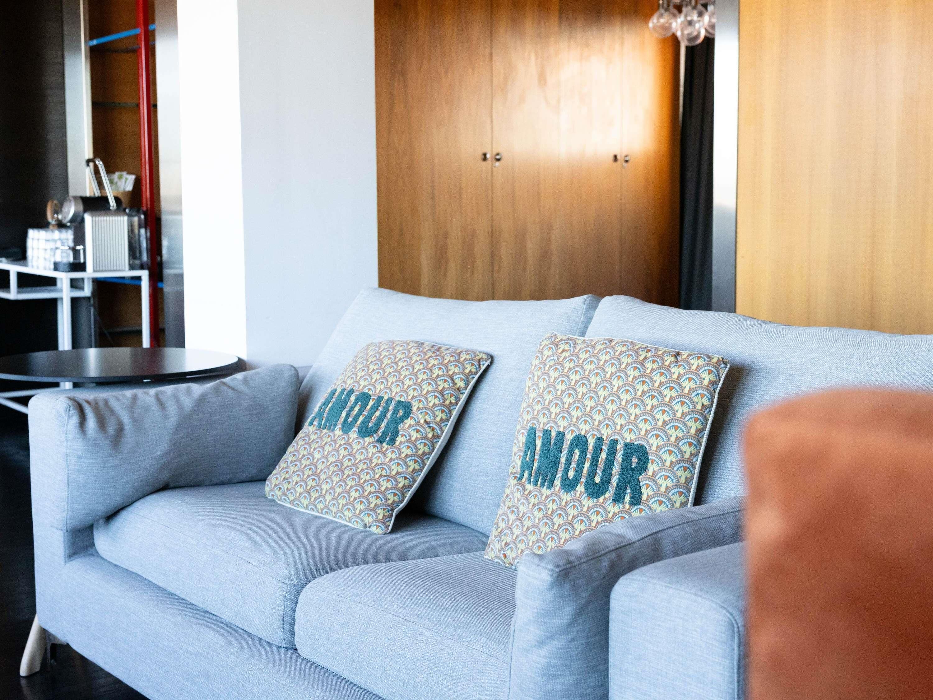 A light blue sofa with two patterned pillows and a wooden wall behind it.