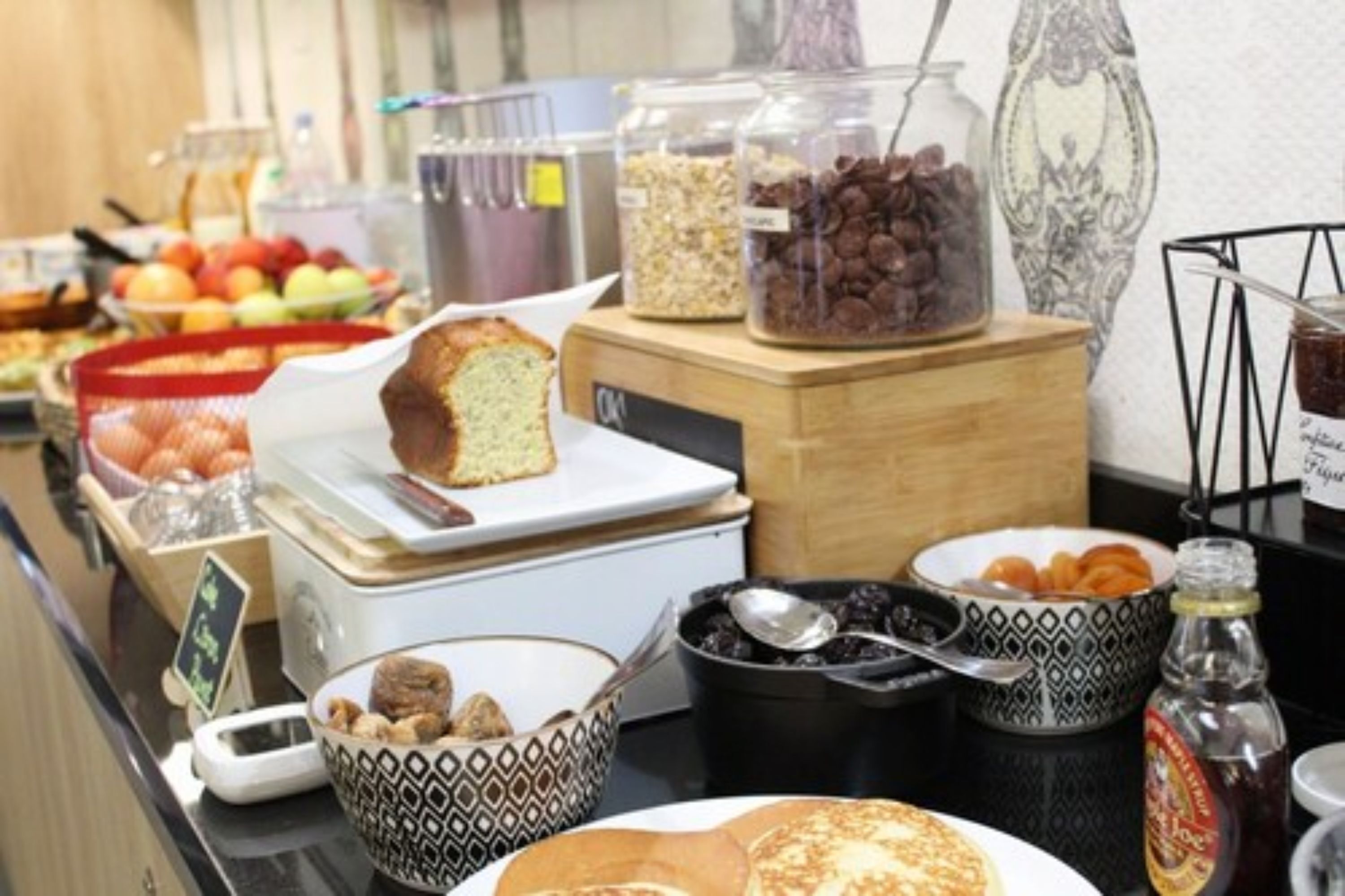 Disposição de buffet com diversos alimentos, incluindo um pão, tigelas de frutas e recipientes com nozes e gotas de chocolate.