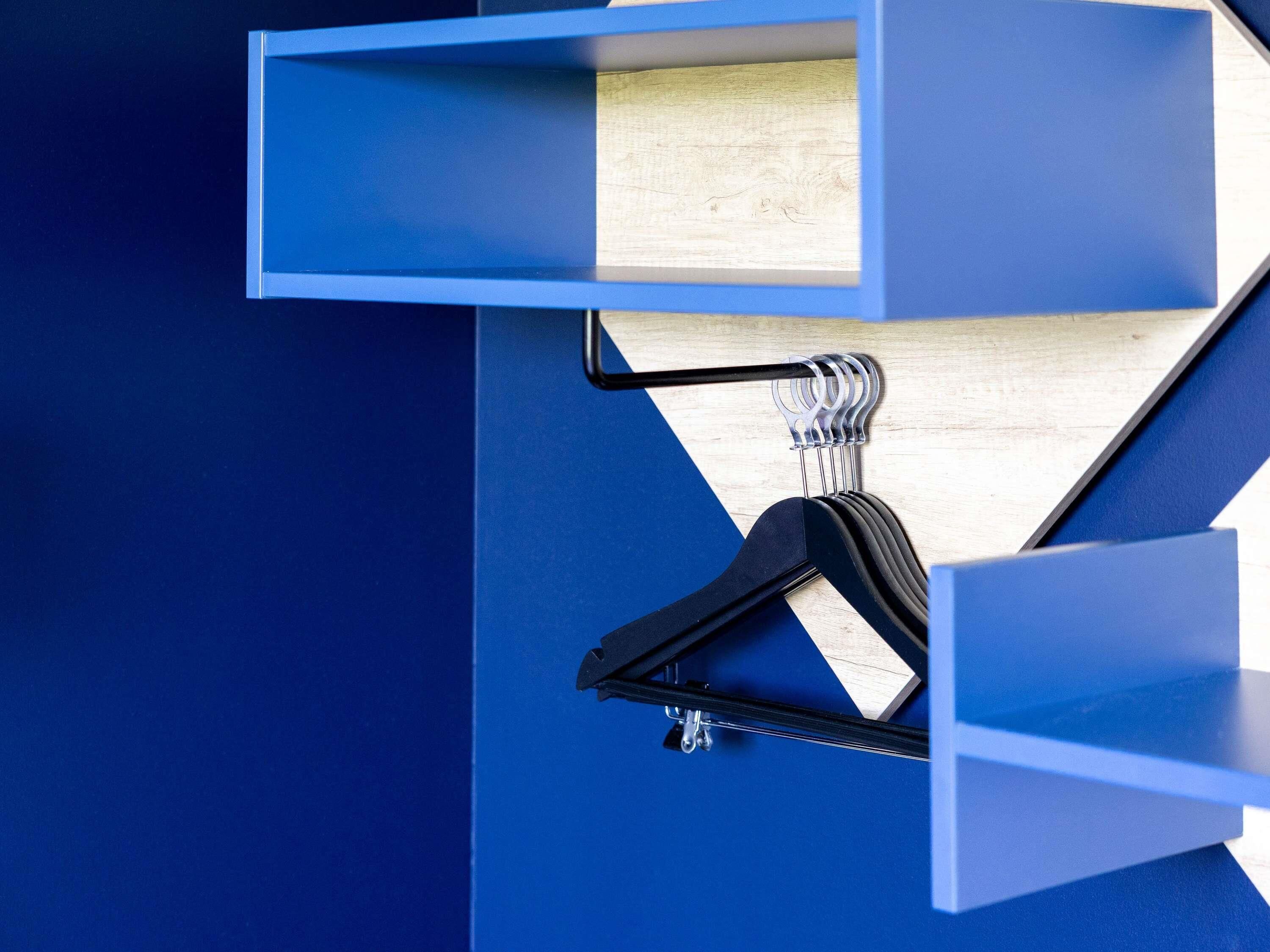 Un mur bleu avec une étagère en bois et un cintre noir.