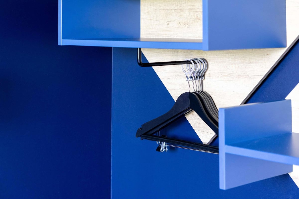 A blue wall with a wooden shelf and a black hanger.