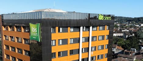 Un moderno edificio de hotel con varios pisos, grandes ventanales y un llamativo letrero verde que indica que pertenece a la cadena ibis Styles.