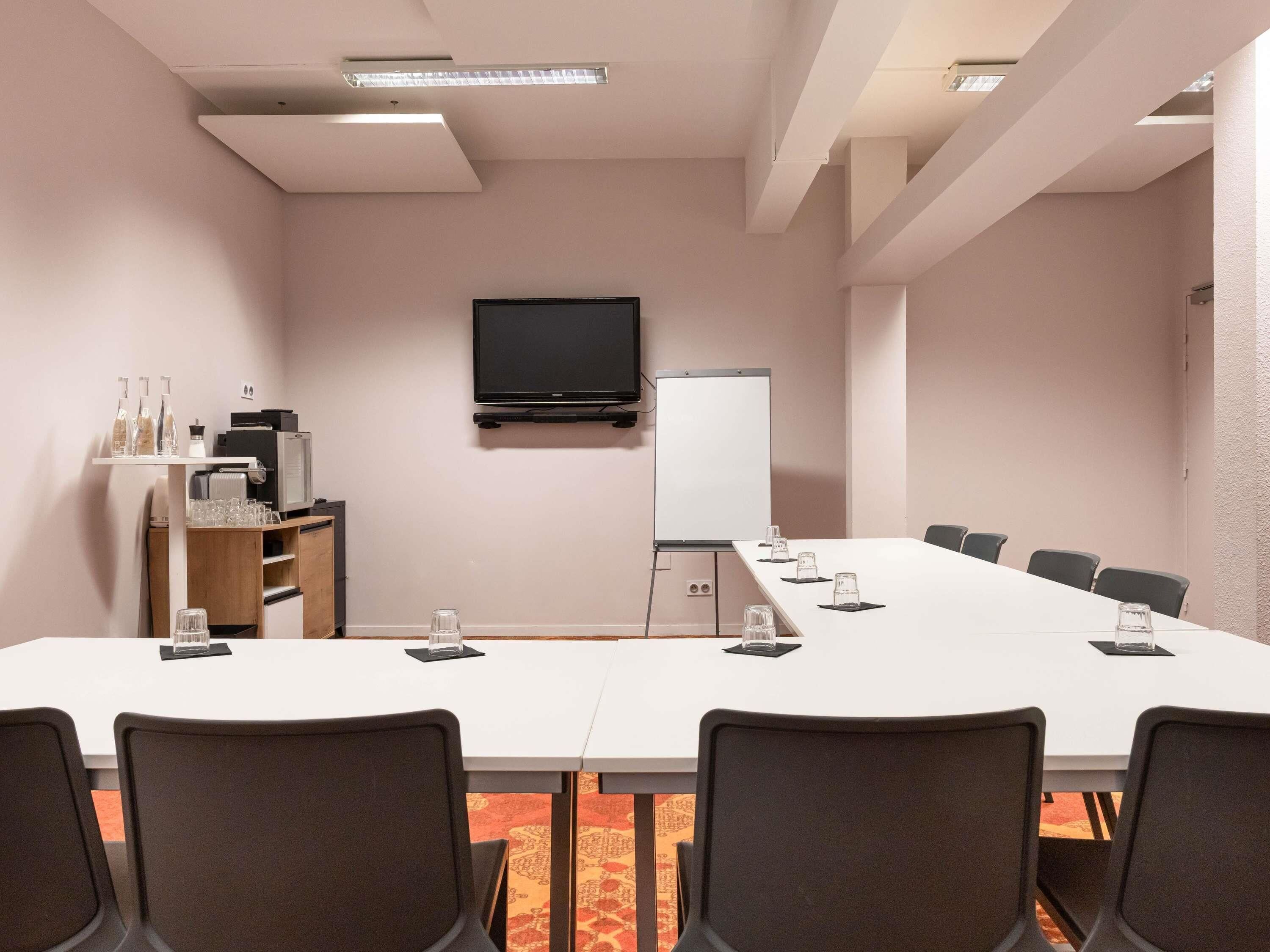 Ein Konferenzraum mit langem Tisch, Stühlen, einem Fernseher, einer Whiteboard und einer Kaffeestation.