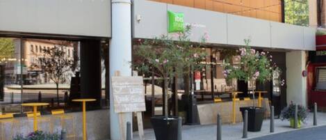 A modern building with a green sign for 'ibis' and outdoor seating.