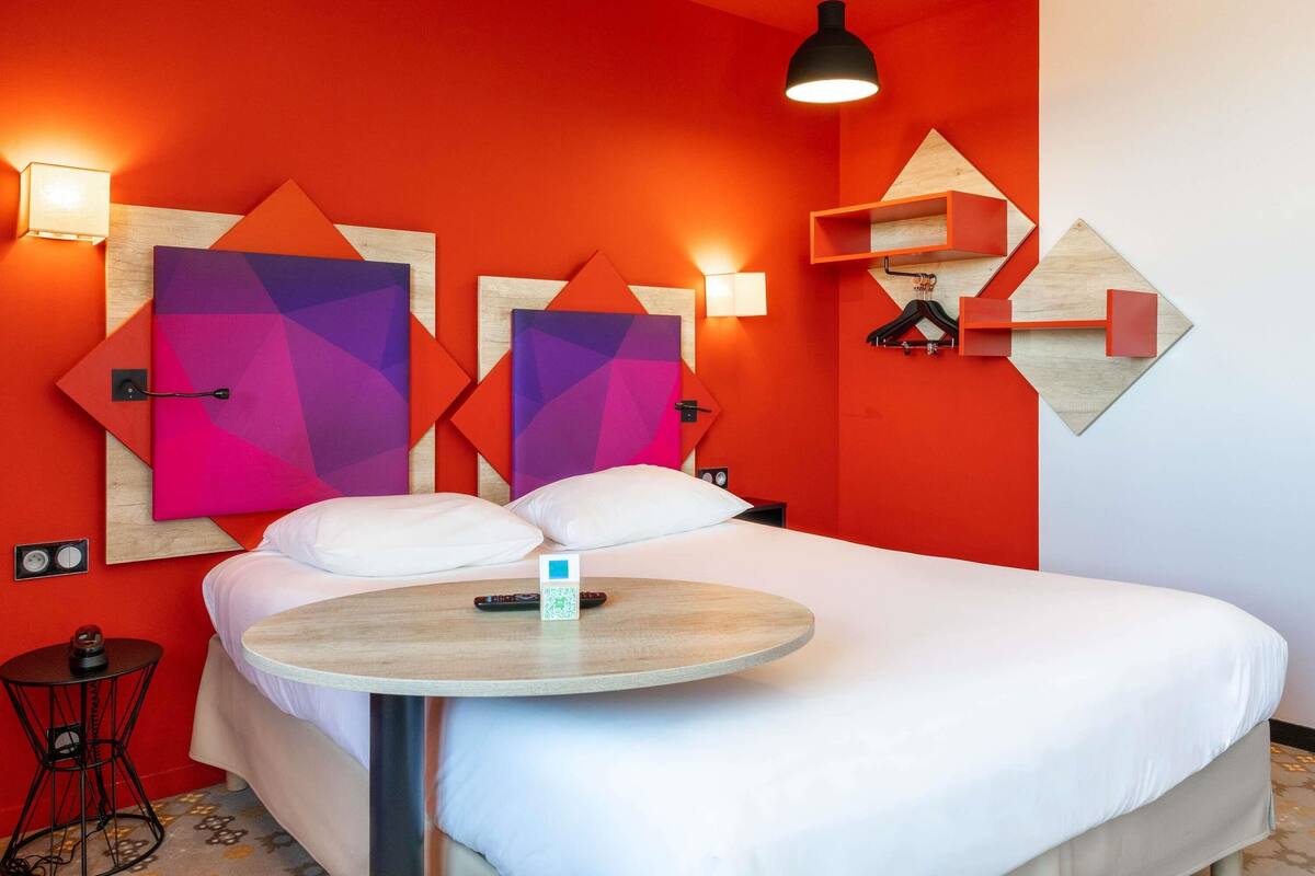 A modern hotel room with a bed, a round table, and geometric wall art.