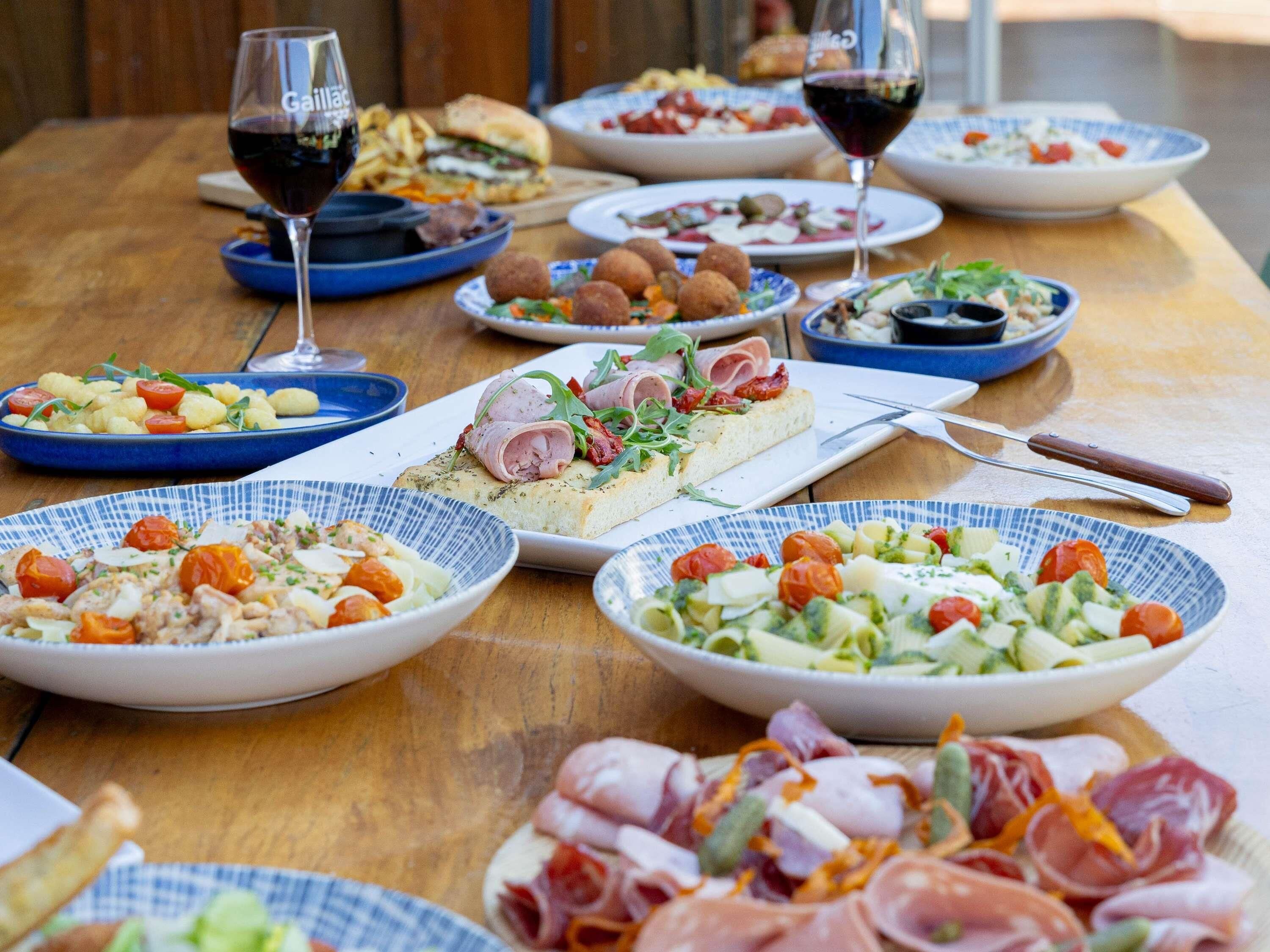 Ein Holztisch mit verschiedenen Gerichten, darunter Salate, Fleisch und Brot, was auf eine Mahlzeit hindeutet.