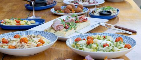 Ein Holztisch mit verschiedenen Gerichten, darunter Salate, Fleisch und Brot, was auf eine Mahlzeit hindeutet.