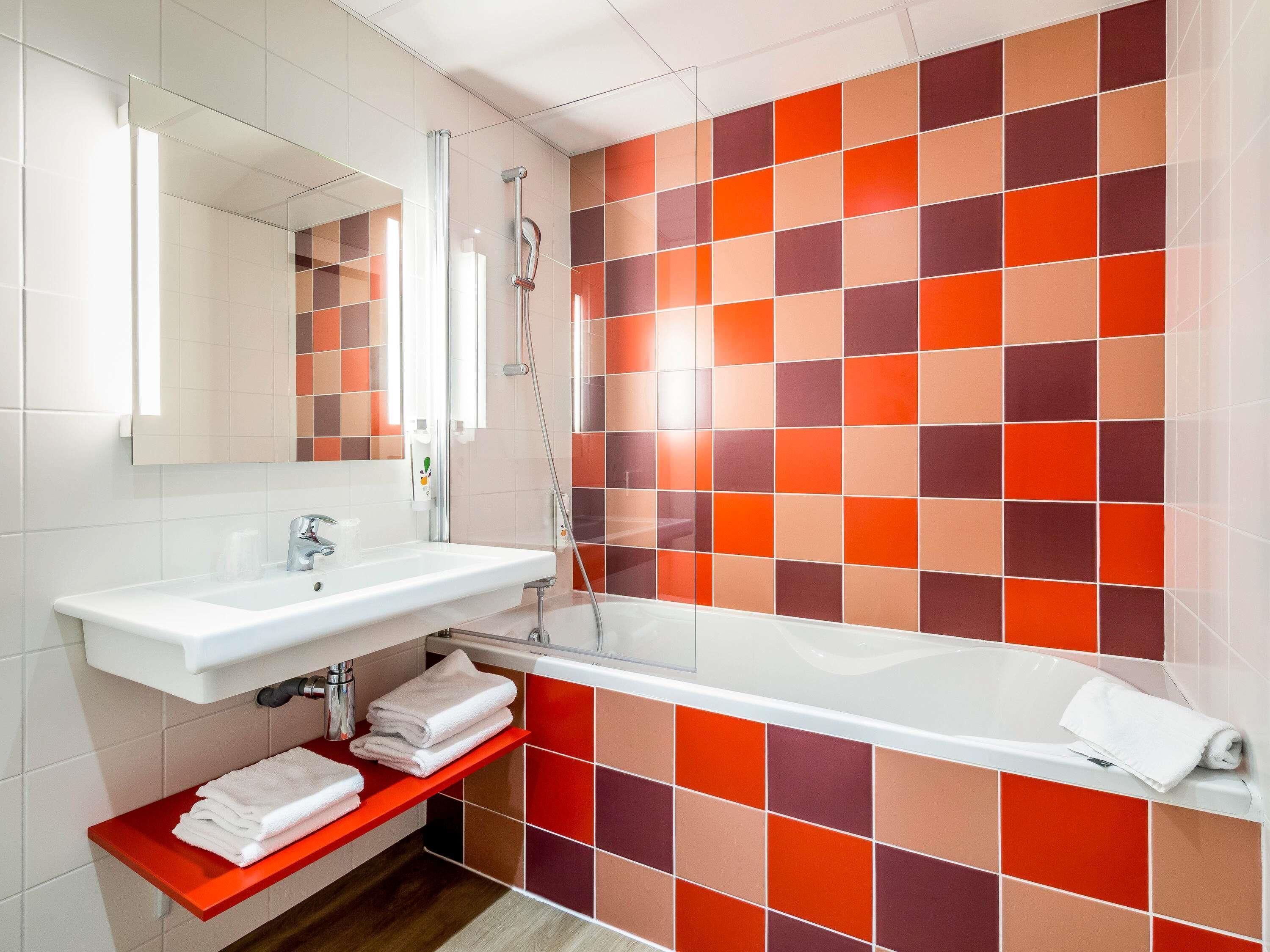 Een badkamer met een wit wastafelmeubel, een spiegel, een douche en een rode plank met handdoeken.