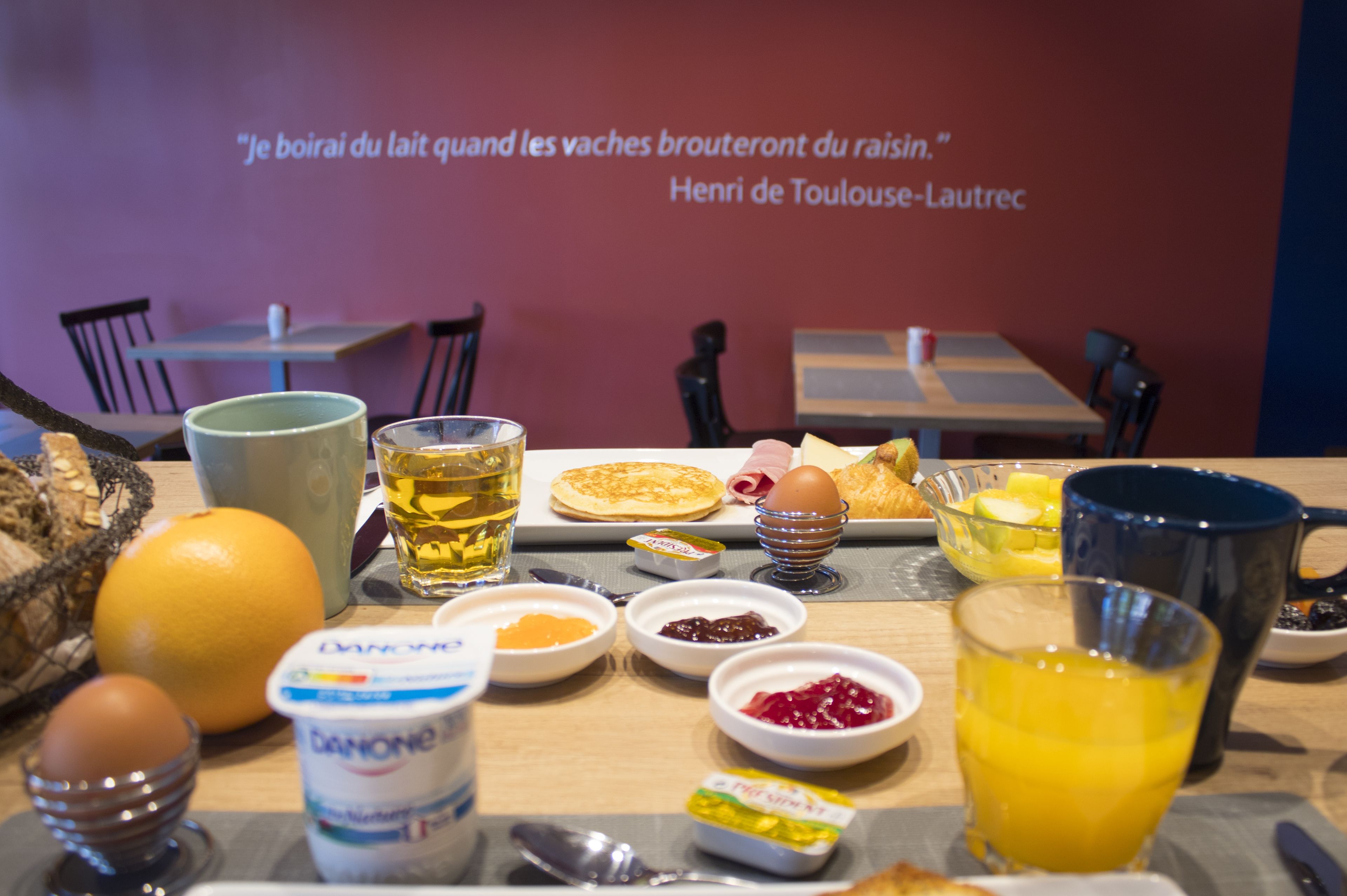A breakfast table with various food items, a glass of orange juice, and a quote on the wall.