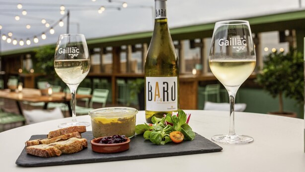 A table with a bottle of Barolo wine, two glasses of white wine, a small bowl of olives, and a plate of bread. - Ibis Styles Albi Centre Le Theatro (Albi)