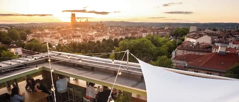 Terraza en la azotea con vistas a un paisaje urbano al atardecer, destacando una torre imponente.