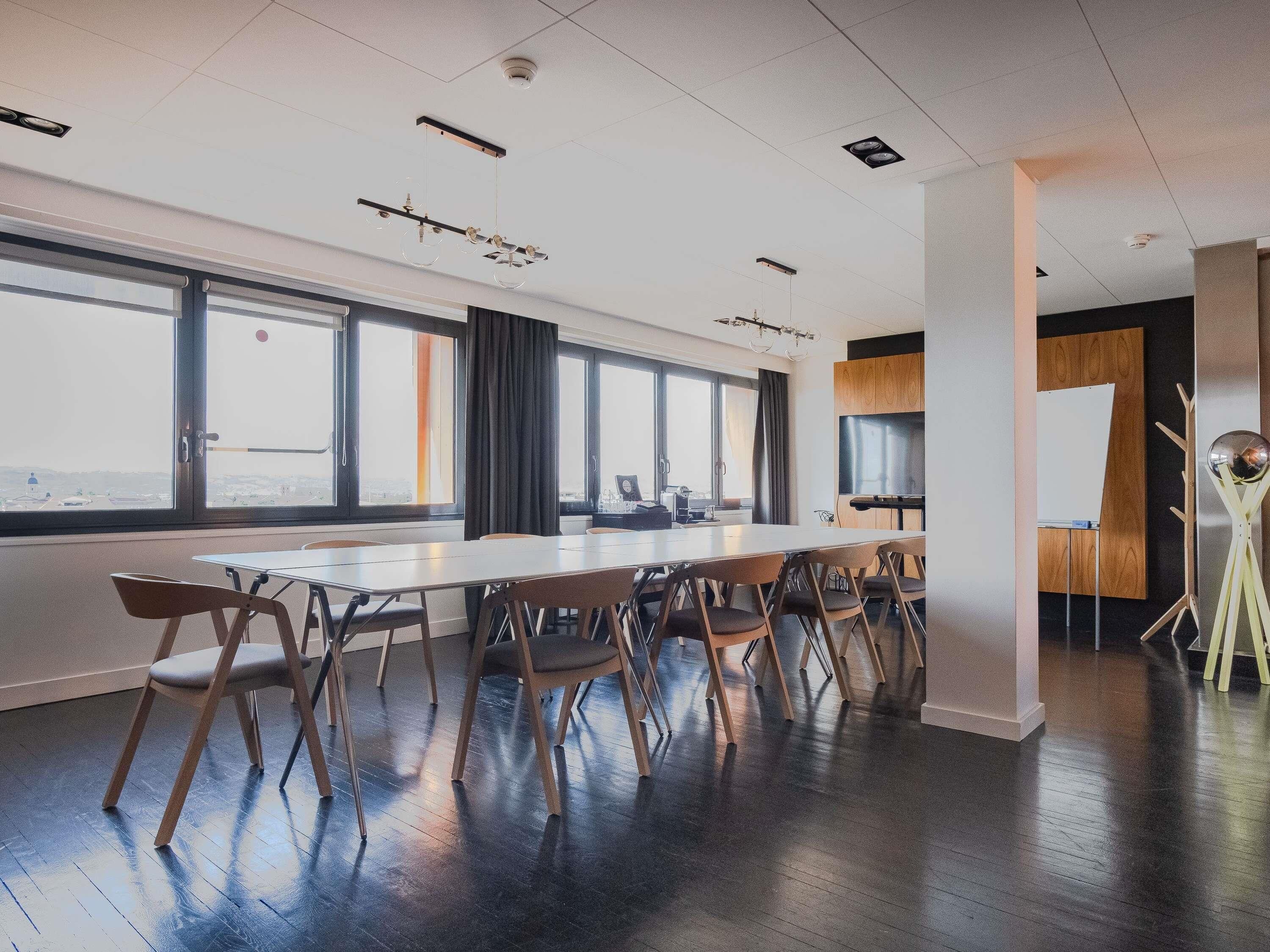 A conference room with a long table, chairs, large windows, and a whiteboard.
