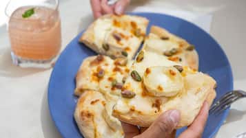 En person holder et pizzastykke med ost og nødder på en blå tallerken.