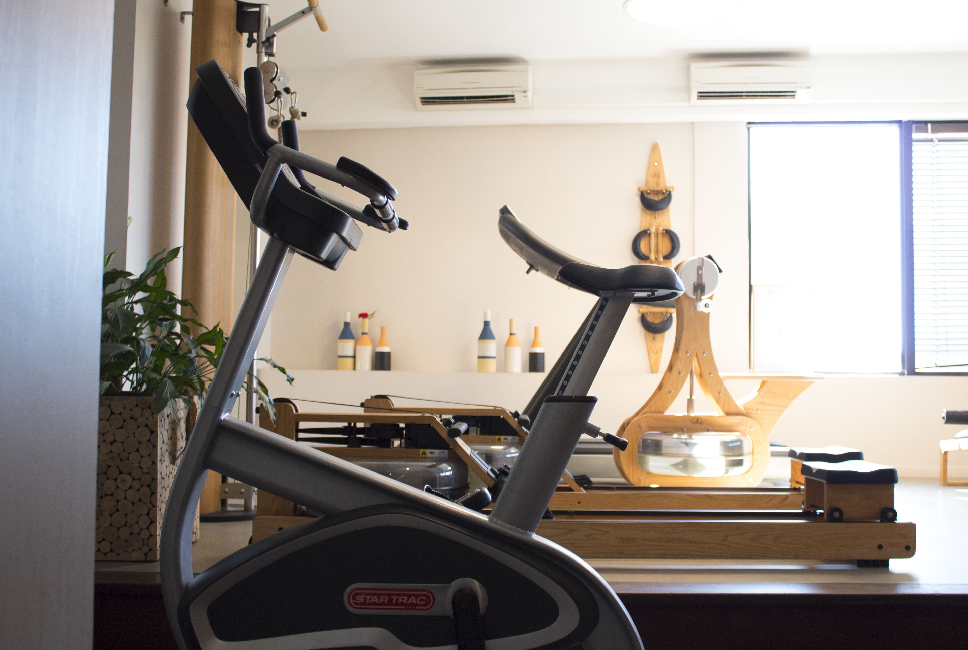Un gimnasio con dos bicicletas estáticas, una escultura de madera y una ventana con persianas.