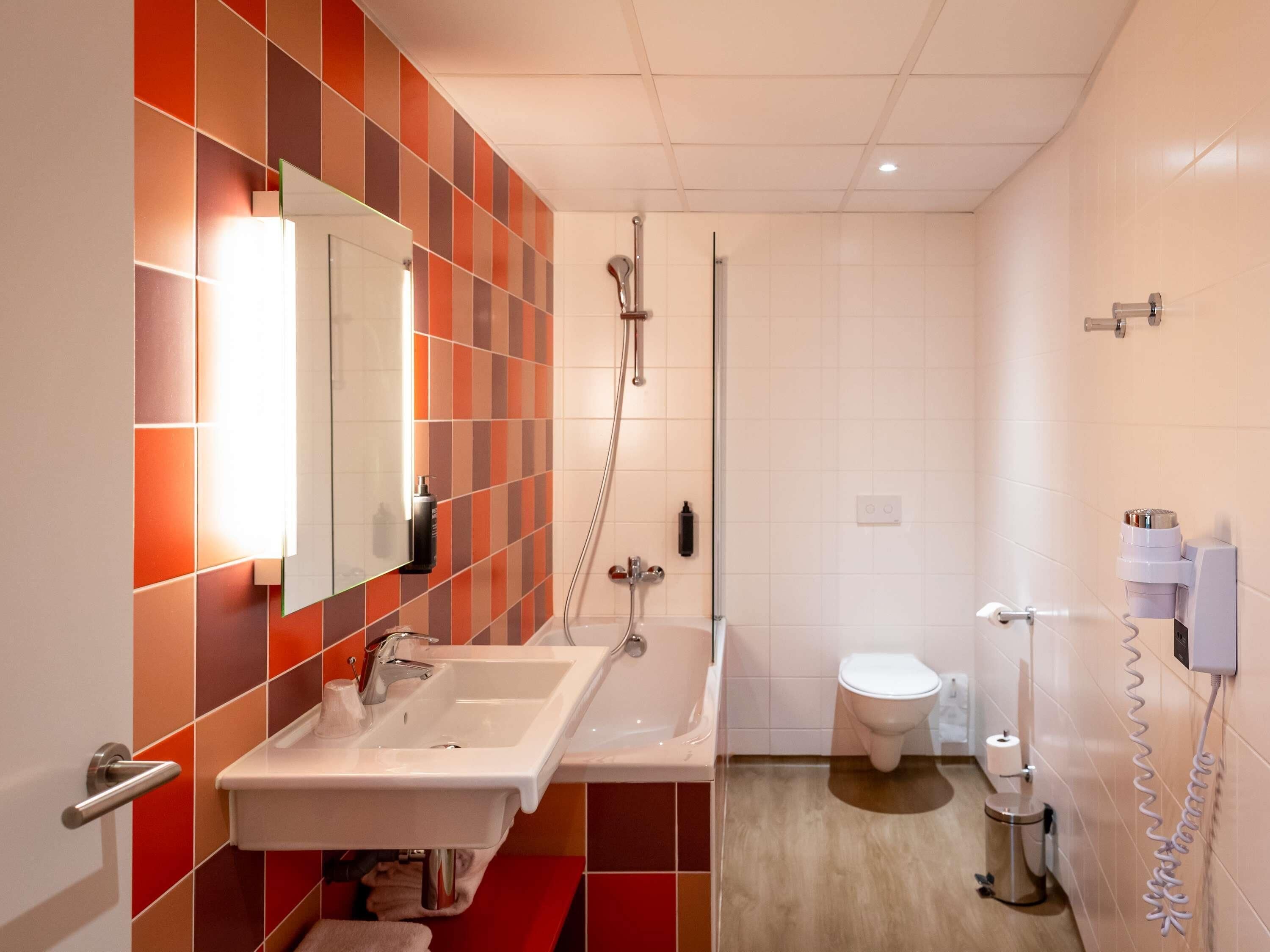 A modern bathroom with a sink, mirror, shower, toilet, and a towel rack.