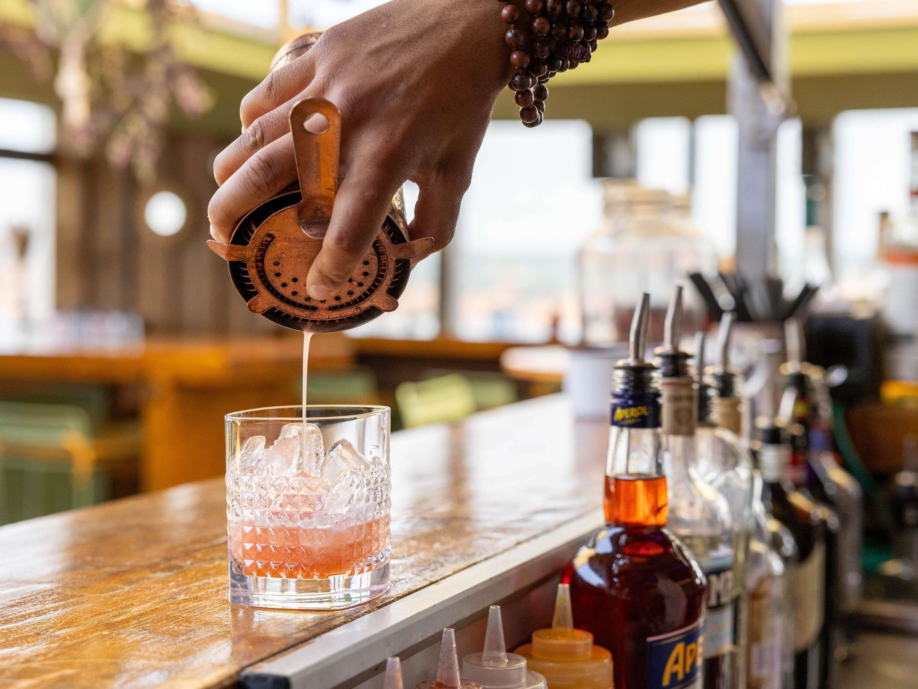 A hand squeezing a citrus fruit into a glass with ice.