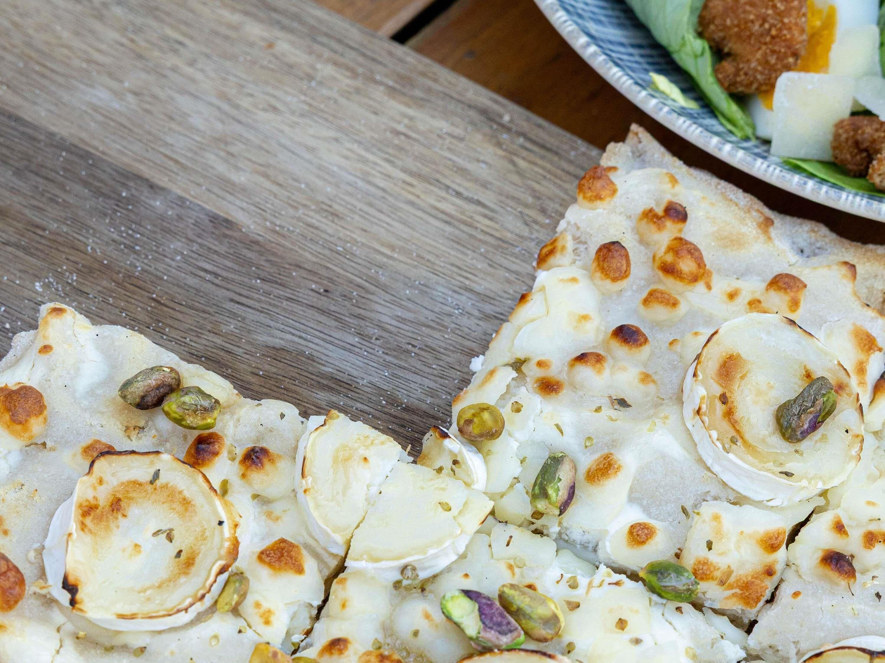 A close-up of a food item with a crispy texture, possibly a type of flatbread or pastry, with visible nuts and a golden-brown crust.